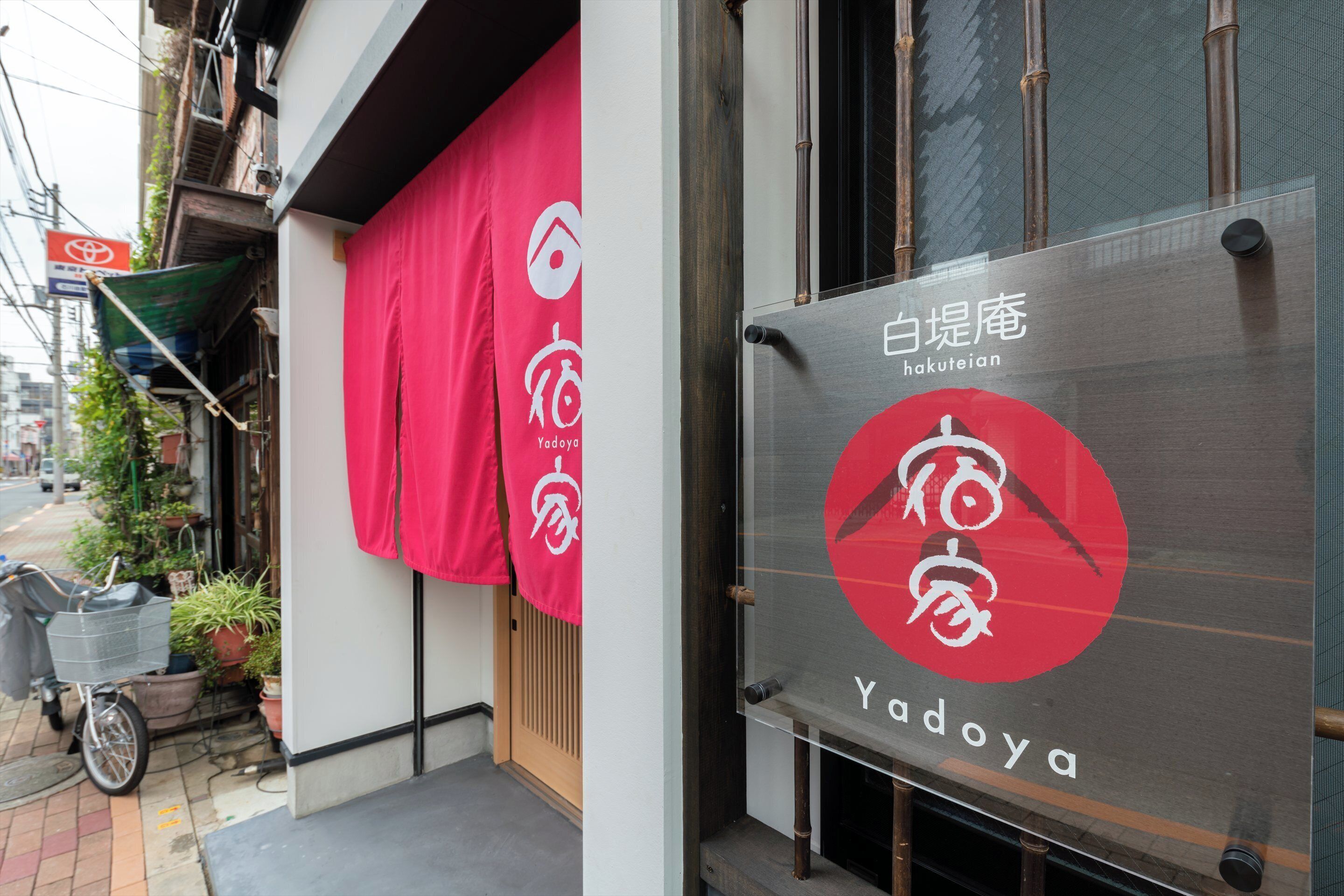 A storefront with a red awning, a metal sign with the name 'Yadoya,' and a bicycle parked outside.
