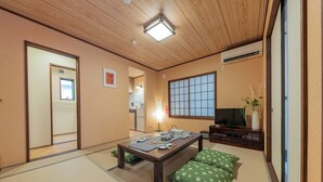 A traditional Japanese-style room with tatami flooring, a low table set for dining, a television, and a sliding door leading to a kitchen. - Yadoya Hakutei-An (Tokyo)