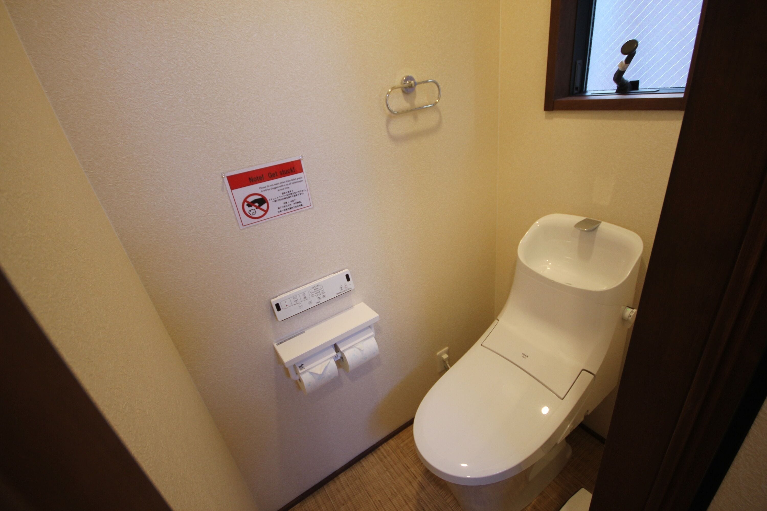Une petite salle de bain propre, équipée de toilettes, d’un distributeur d’essuie-tout et d’un sèche-mains.