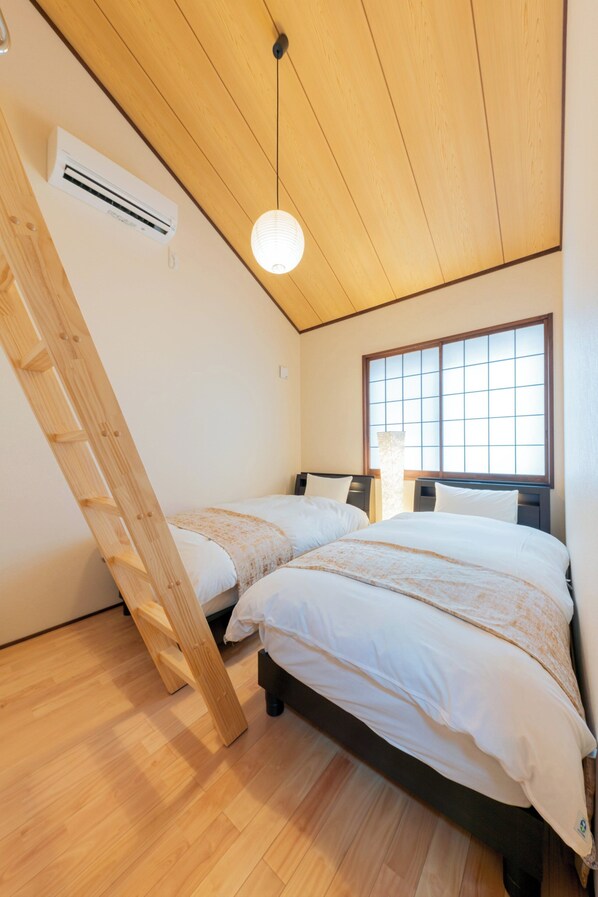 Habitación con dos camas, una escalera de madera, un ventanal con diseño de cuadrícula y un equipo de aire acondicionado.