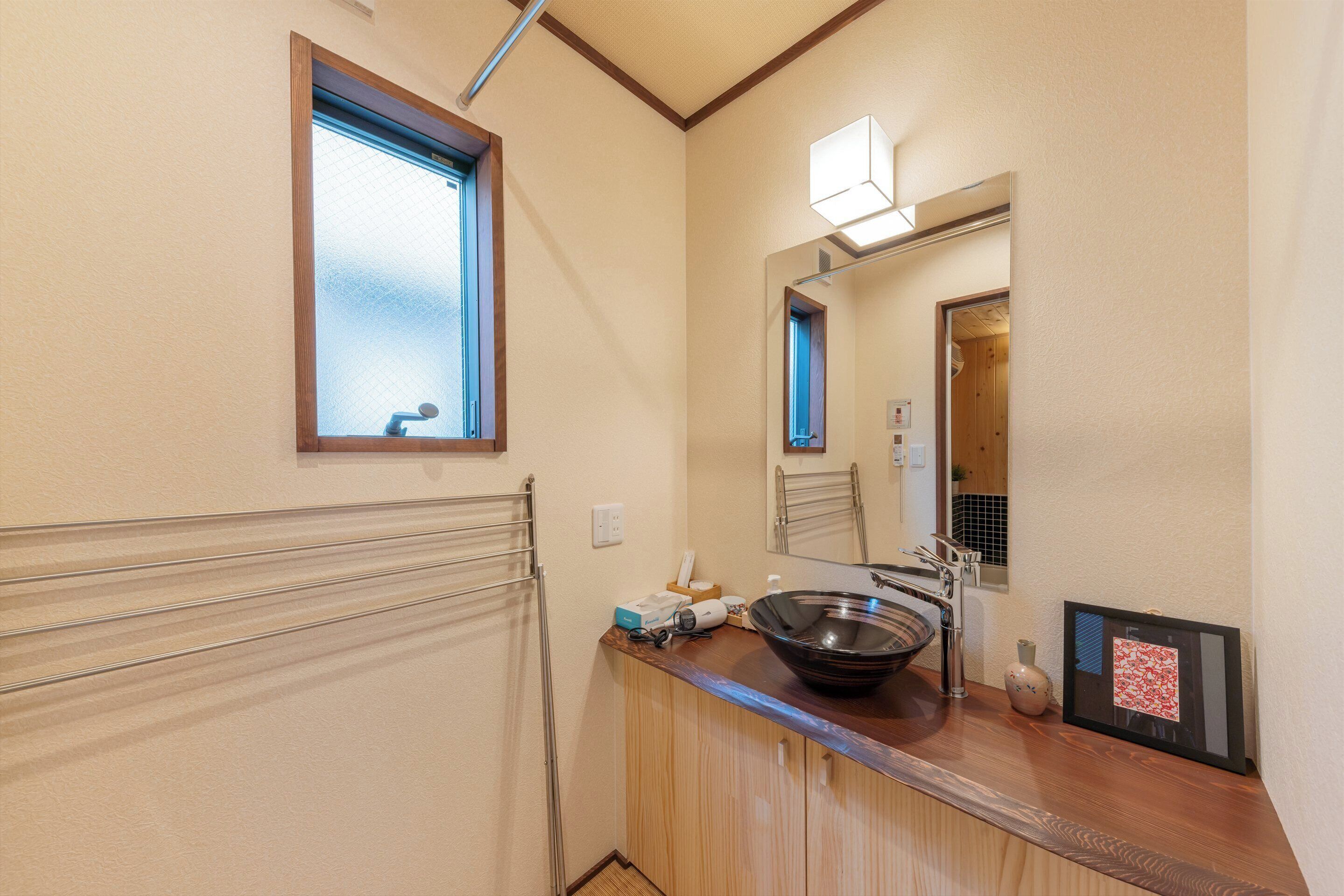 Ein Badezimmer mit einem Holzwaschtisch, einem großen Spiegel, einem Fenster und einem gerahmten Bild an der Wand.