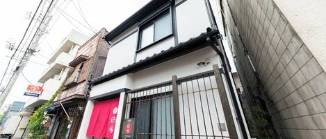 Un bâtiment à deux étages, avec une entrée visible au rez-de-chaussée, un vélo garé à l’extérieur et un auvent rouge.