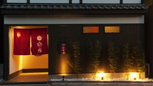 Ein traditionelles japanisches Gebäude mit Holzfassade, rotem Eingangsvorbau und einem Schild mit japanischen Schriftzeichen.