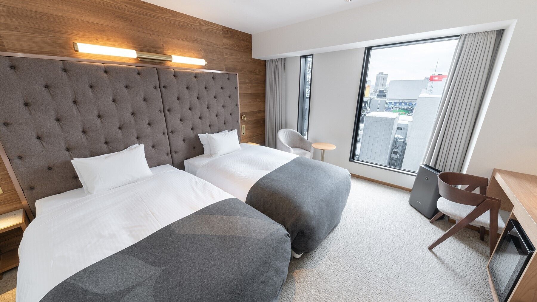 Une chambre d’hôtel avec deux lits, une tête de lit en bois, un bureau et une chaise.