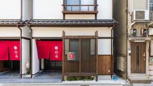 Ein traditionelles japanisches Gebäude mit einem hölzernen Eingangstor, roten Markisen und einem kleinen Garten.