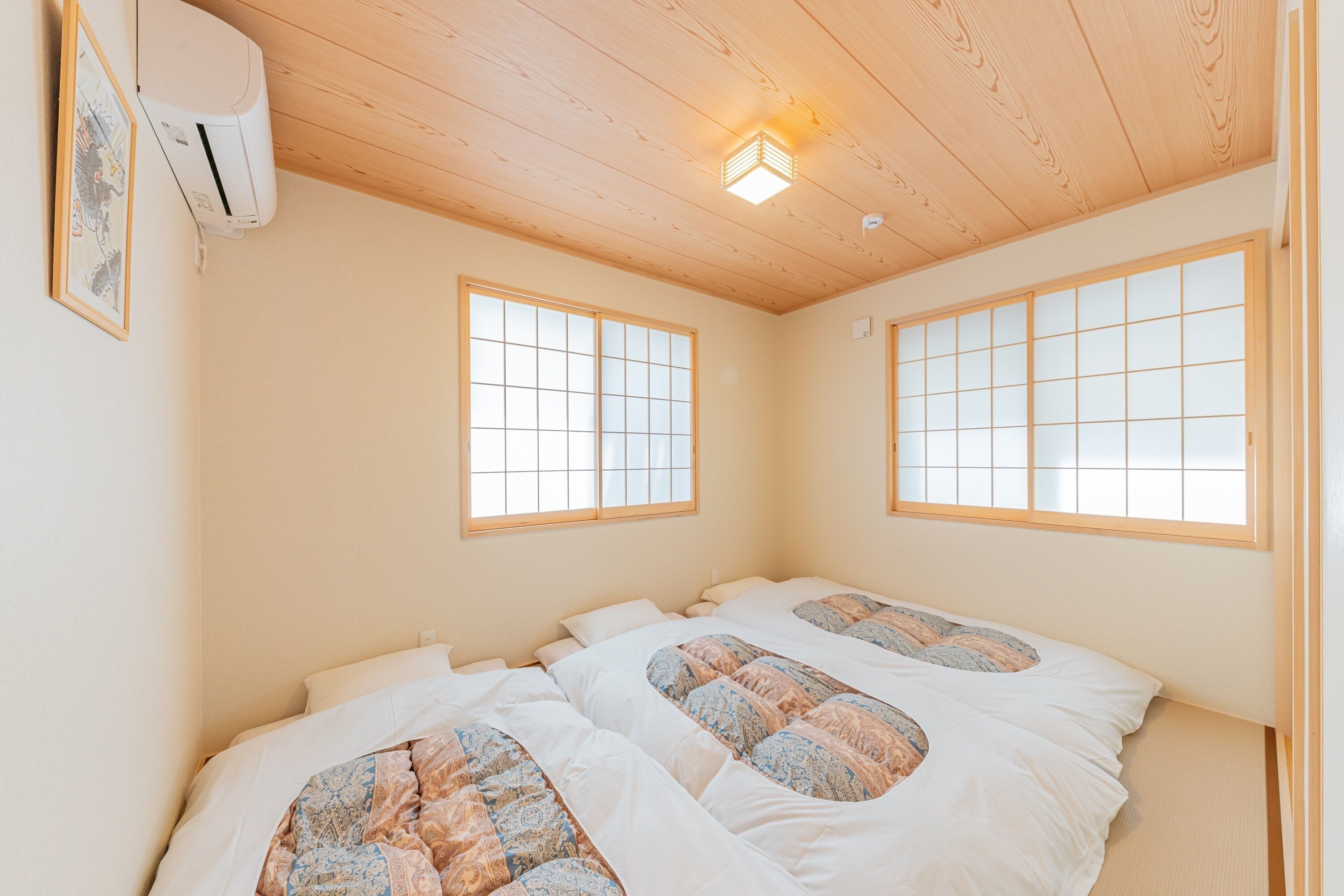 A room with two beds, a ceiling fan, and a window with a grid pattern.