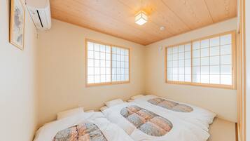 A room with two beds, a ceiling fan, and a window with a grid pattern.