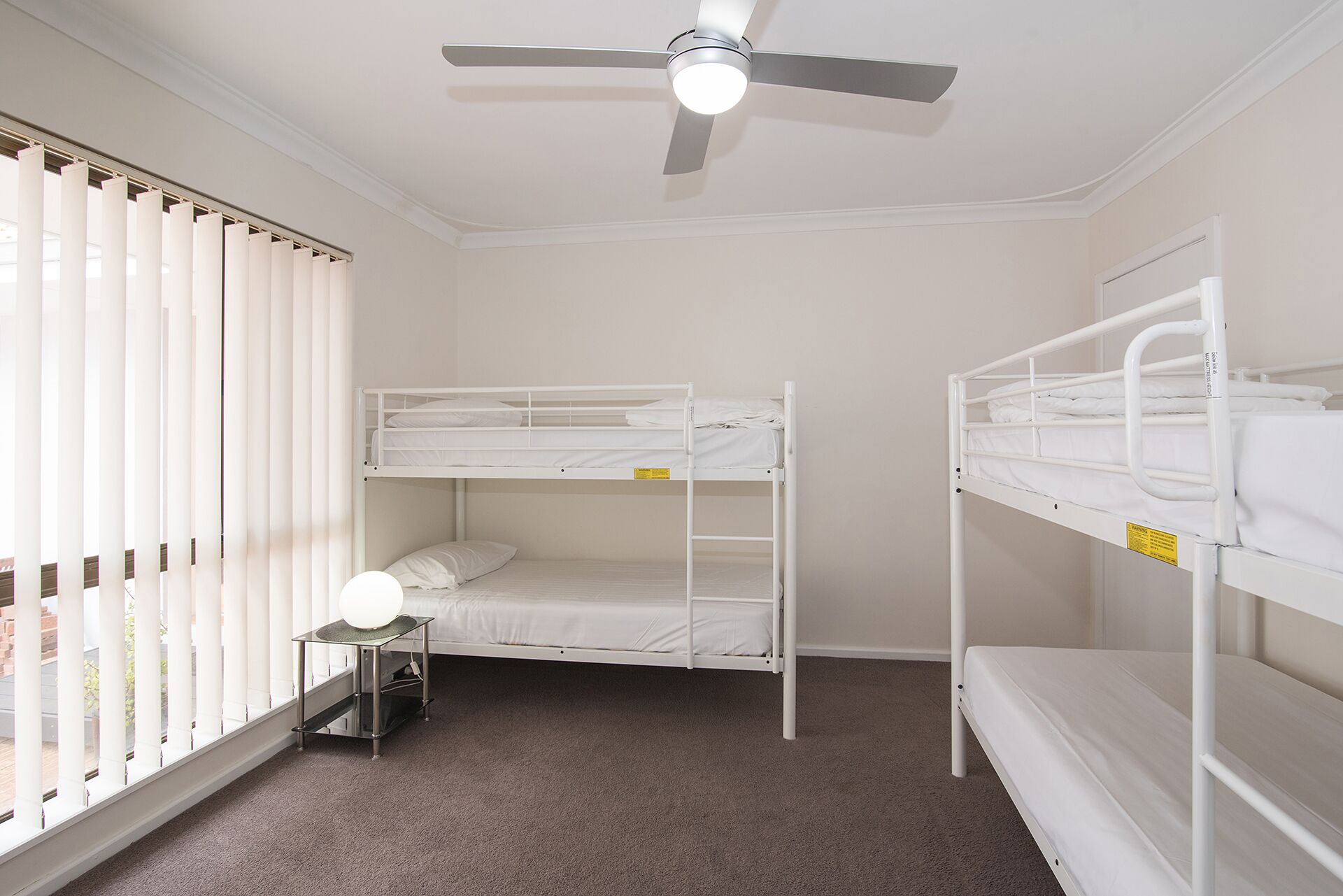 A room with two bunk beds, a ceiling fan, and a small table with a lamp.