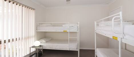 A room with two bunk beds, a ceiling fan, and a small table with a lamp.