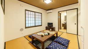 Una tradizionale stanza giapponese con pavimento in tatami, un tavolino con televisore e una porta scorrevole che dà su un'altra stanza.