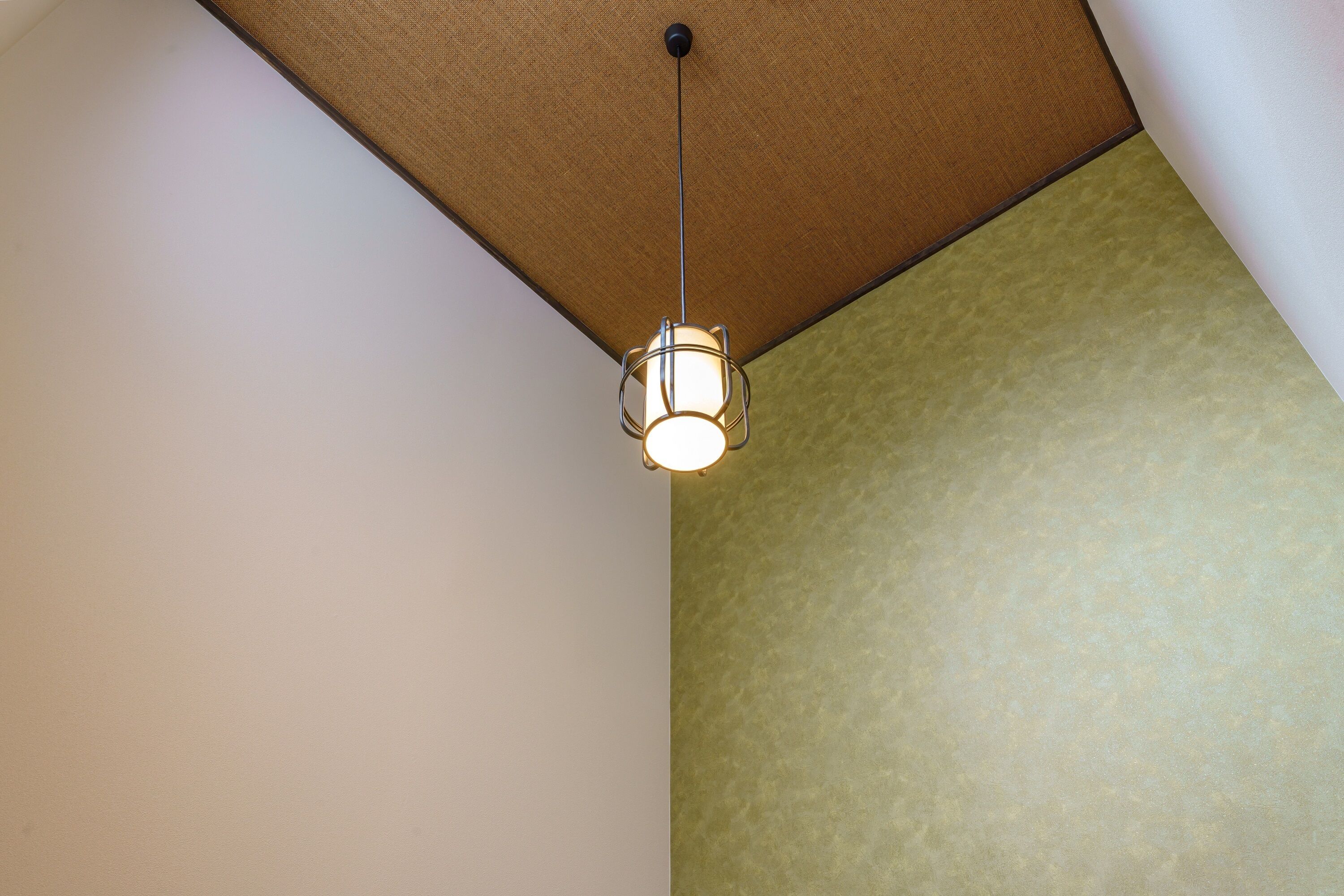 A ceiling with a hanging light fixture and a textured wall.