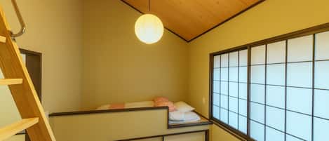 Una habitación pequeña con una litera, una escalera de madera, un panel shoji y un farol de papel colgante.