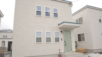 A two-story building with a light-colored exterior, a green door, and a small porch area.