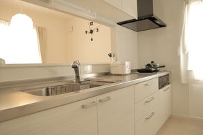 A modern kitchen with a stainless steel sink, white cabinets, a built-in oven, and a black range hood. - Bayside Hakodate (Hakodate)