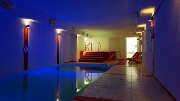 An indoor swimming pool with a clear water surface, a red chair, and a staircase leading to a higher level. - Akwamaryn Spa Niechorze (Rewal)