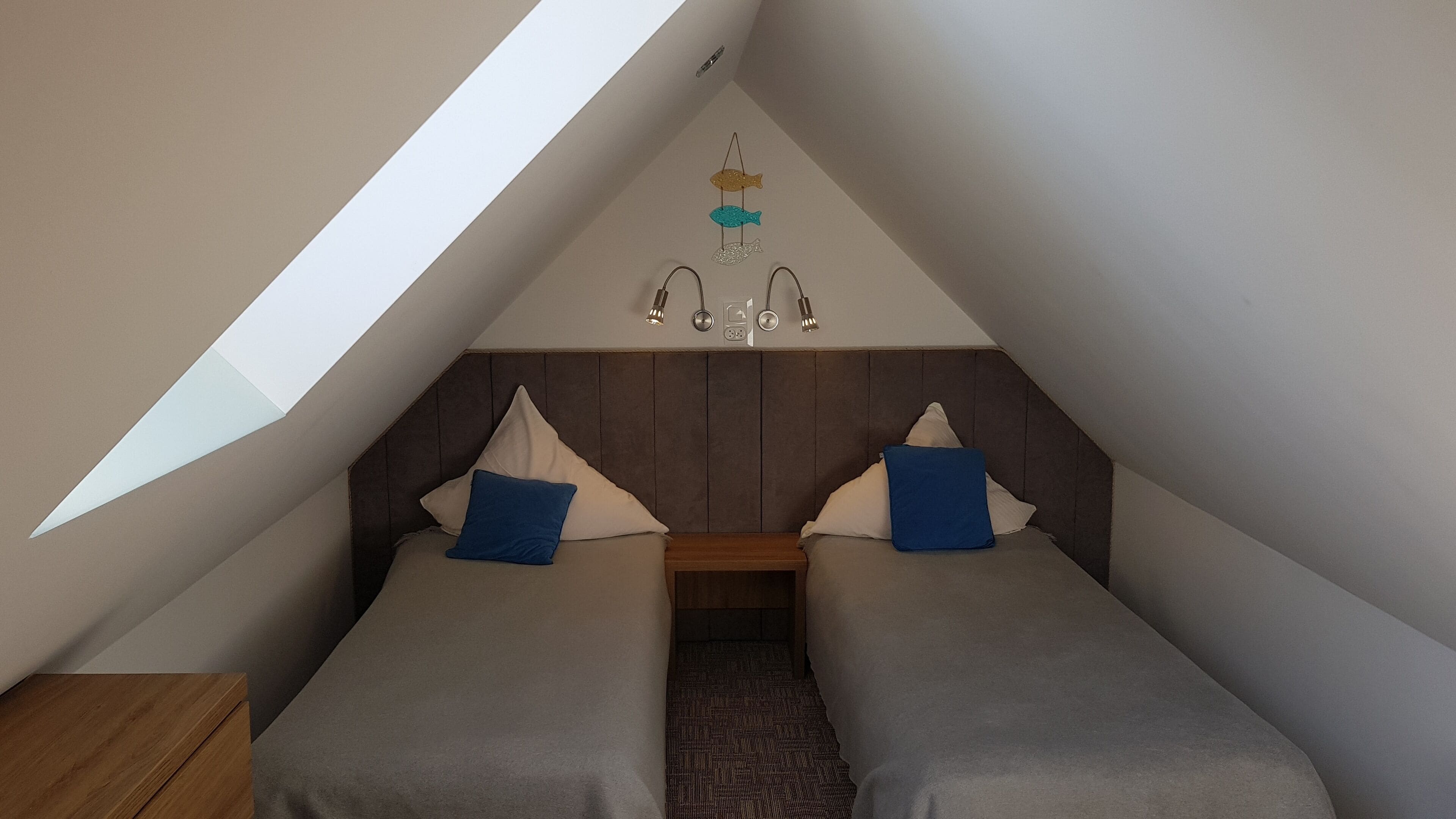 Ein Schlafzimmer mit zwei Betten, einem Nachttisch aus Holz, einer Kandelaberleuchte und einer schrägen Decke.