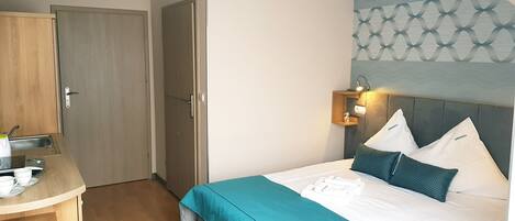 Una habitación de hotel con una cama, un escritorio con silla, una mesita pequeña y un armario.