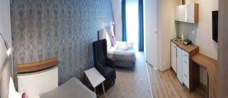 A hotel room with a bed, a desk, a chair, a small table, a wardrobe, a TV, and a bathroom with a shower and toilet.