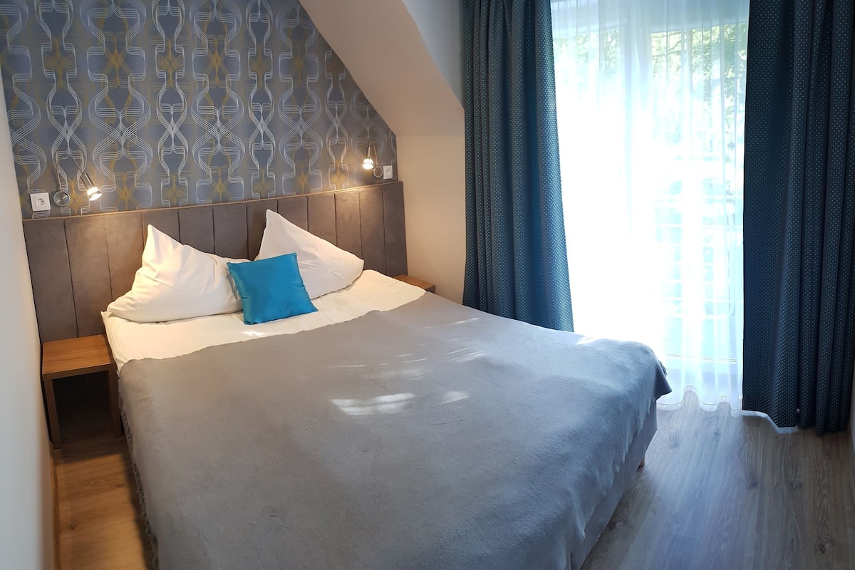 A bedroom with a bed, a headboard, a nightstand, and a window with curtains.