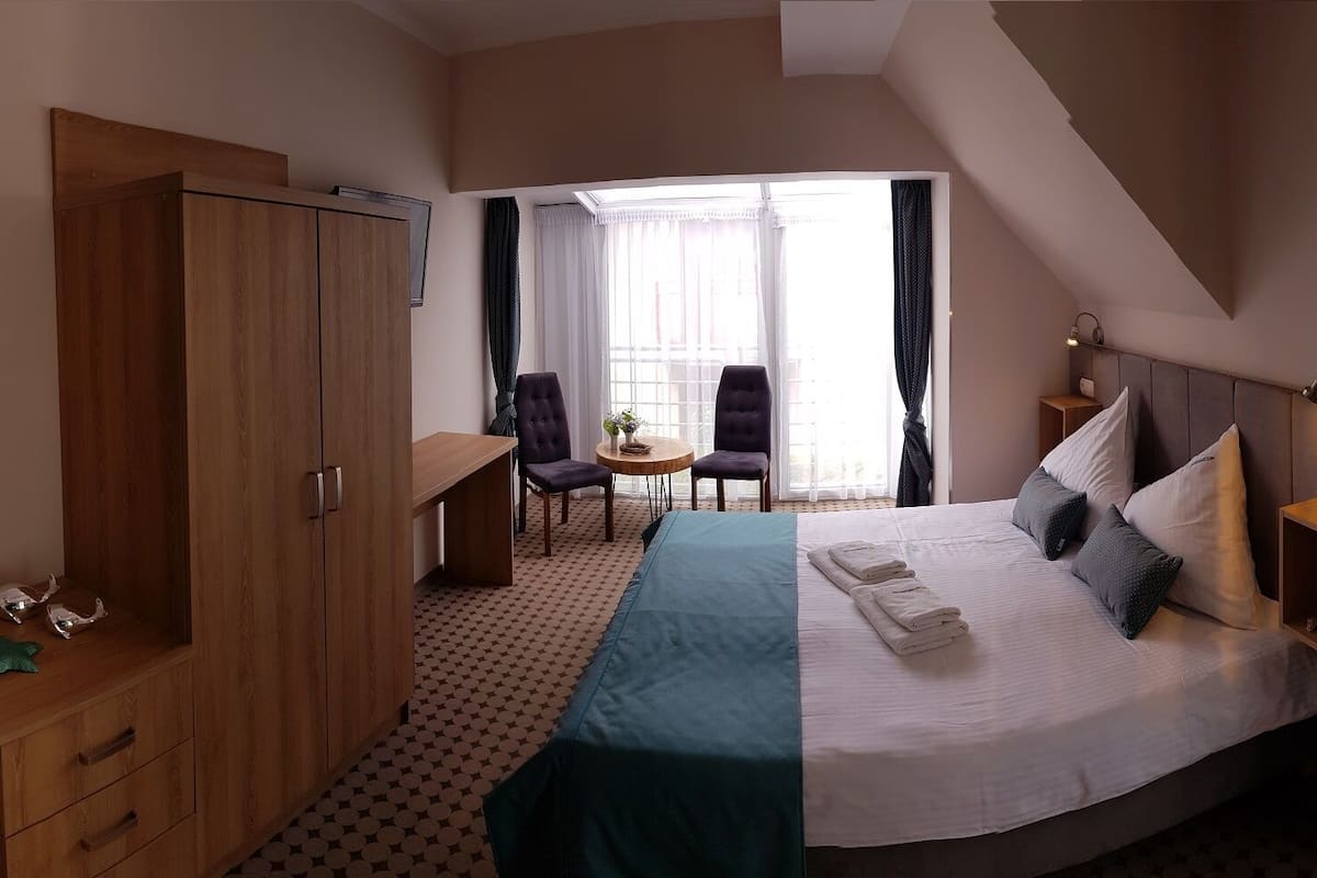 A hotel room with a bed, a desk, a wardrobe, and a small table with chairs.