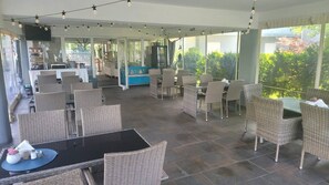An outdoor patio area with wicker furniture, a glass table, and a view of the garden. - Akwamaryn Spa Niechorze (Rewal)