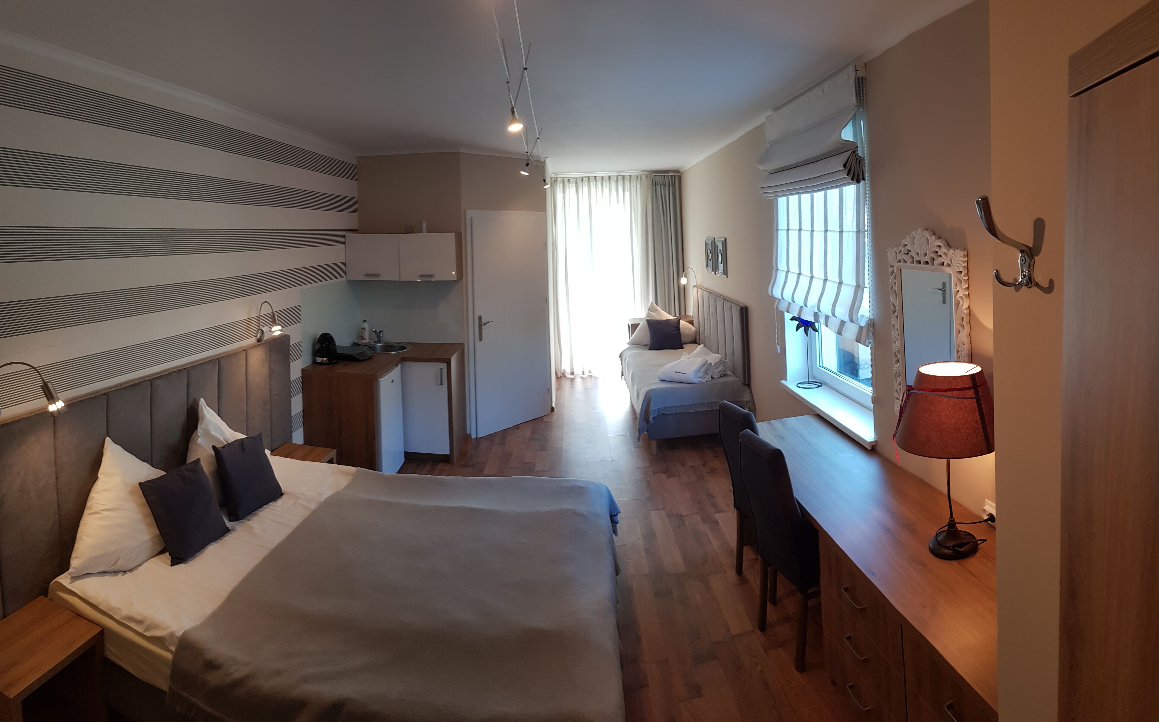 Moderni hotellihuone, jossa on suuri sänky, pieni keittokomero, työpöytä ja ikkuna, jossa on verhot.
