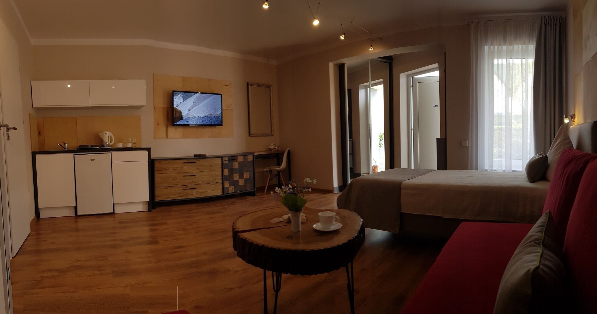 Una habitación de hotel moderna con una cama, un pequeño comedor, un televisor y una kitchenette.