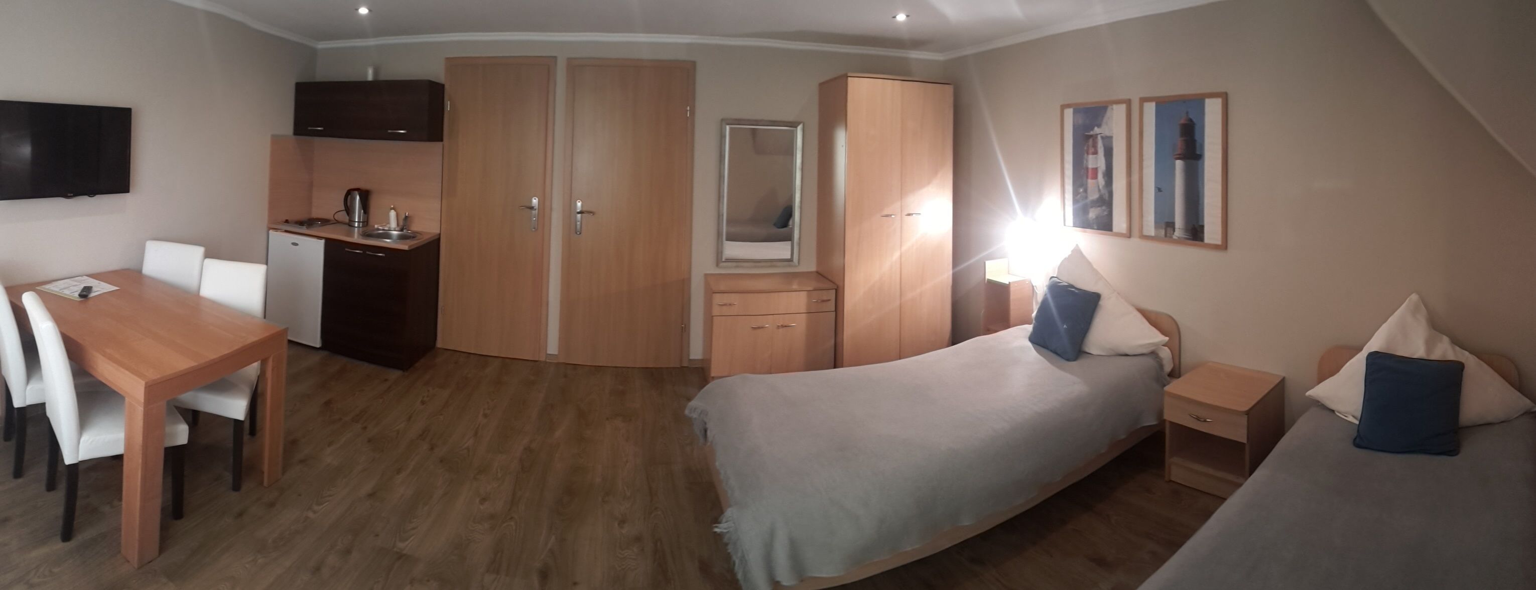 Une chambre de taille modeste comprenant un lit, des tables de chevet, un bureau avec des chaises, une armoire, un miroir et un téléviseur.