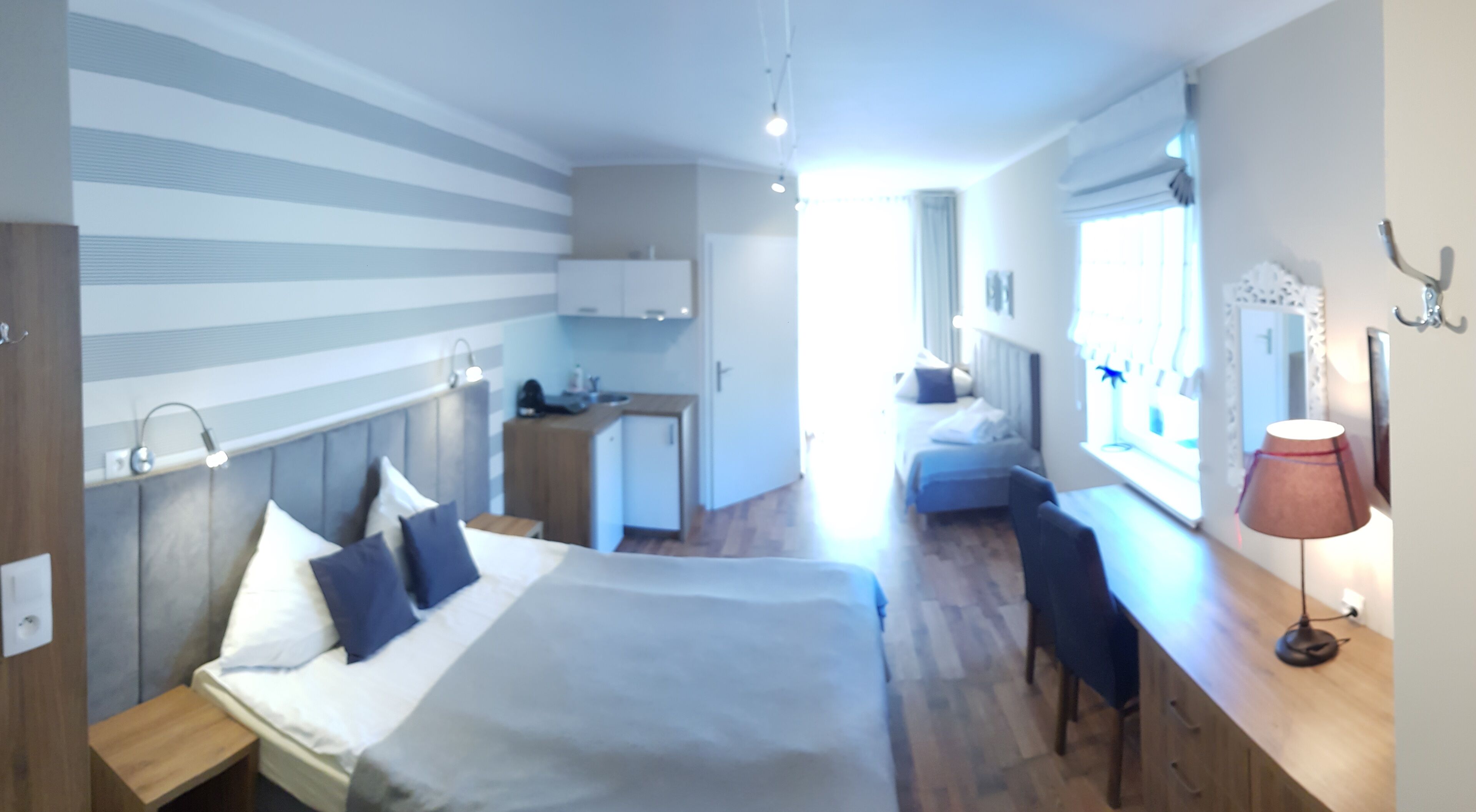 A modern hotel room with a large bed, a desk, a small kitchenette, and a view of the city.