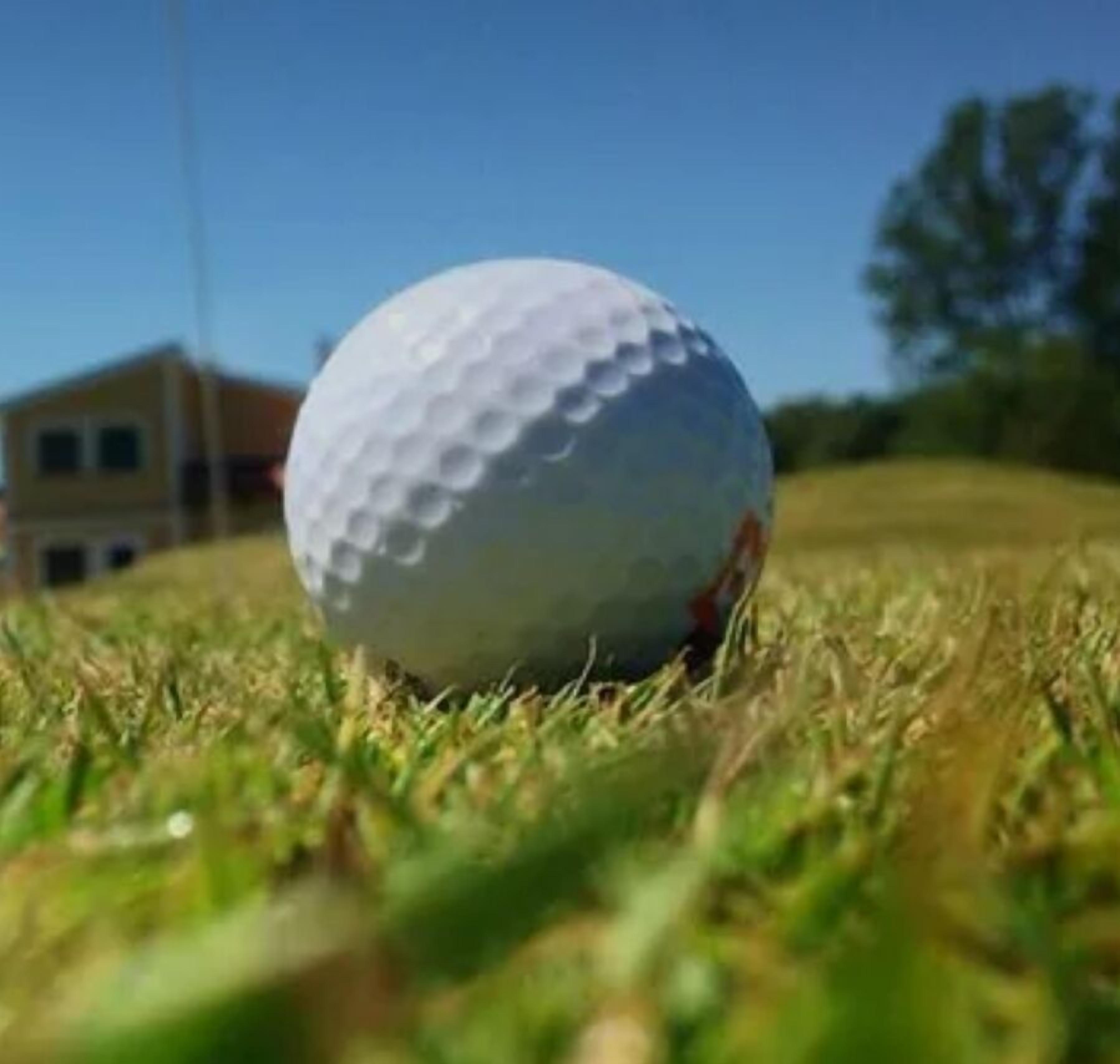 Une balle de golf sur un terrain herbeux, avec un bâtiment en arrière-plan.