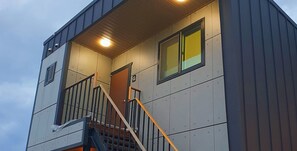 Un edificio moderno con una escalera que conduce a un nivel superior, una puerta marcada con la letra 'G' y un ventanal con vidrio teñido de amarillo.