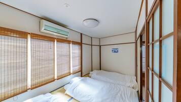 A traditional Japanese-style room with tatami flooring, a futon bed, sliding shoji doors, and a ceiling-mounted air conditioning unit.