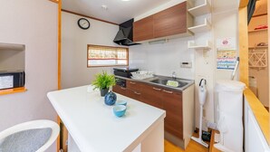 A compact kitchen with a white countertop, wooden cabinets, a sink, and a microwave. - Yadoya Chigusa Cho (Tokyo)