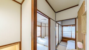 A traditional Japanese-style room with tatami flooring, a wooden-framed sliding door, a small washbasin, and a window with blinds. - Yadoya Chigusa Cho (Tokyo)