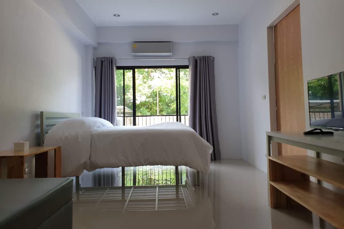 Un dormitorio con cama, escritorio, televisor y ventana con cortinas.