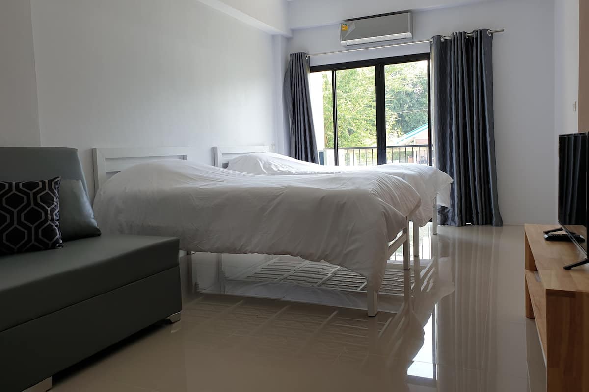 Una habitación de hotel moderna con cama, sofá, mesa de madera y ventana con cortinas.