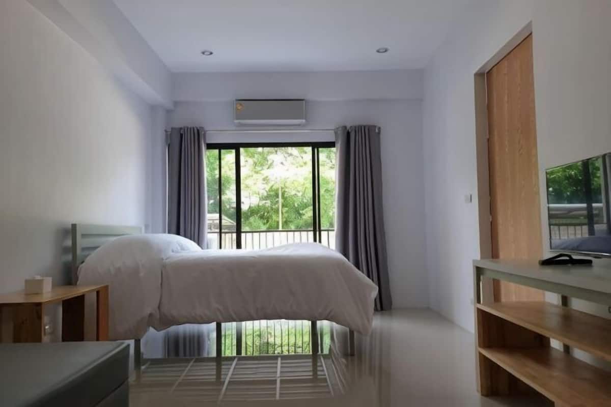 Un dormitorio con cama, televisor, escritorio y ventana con cortinas.