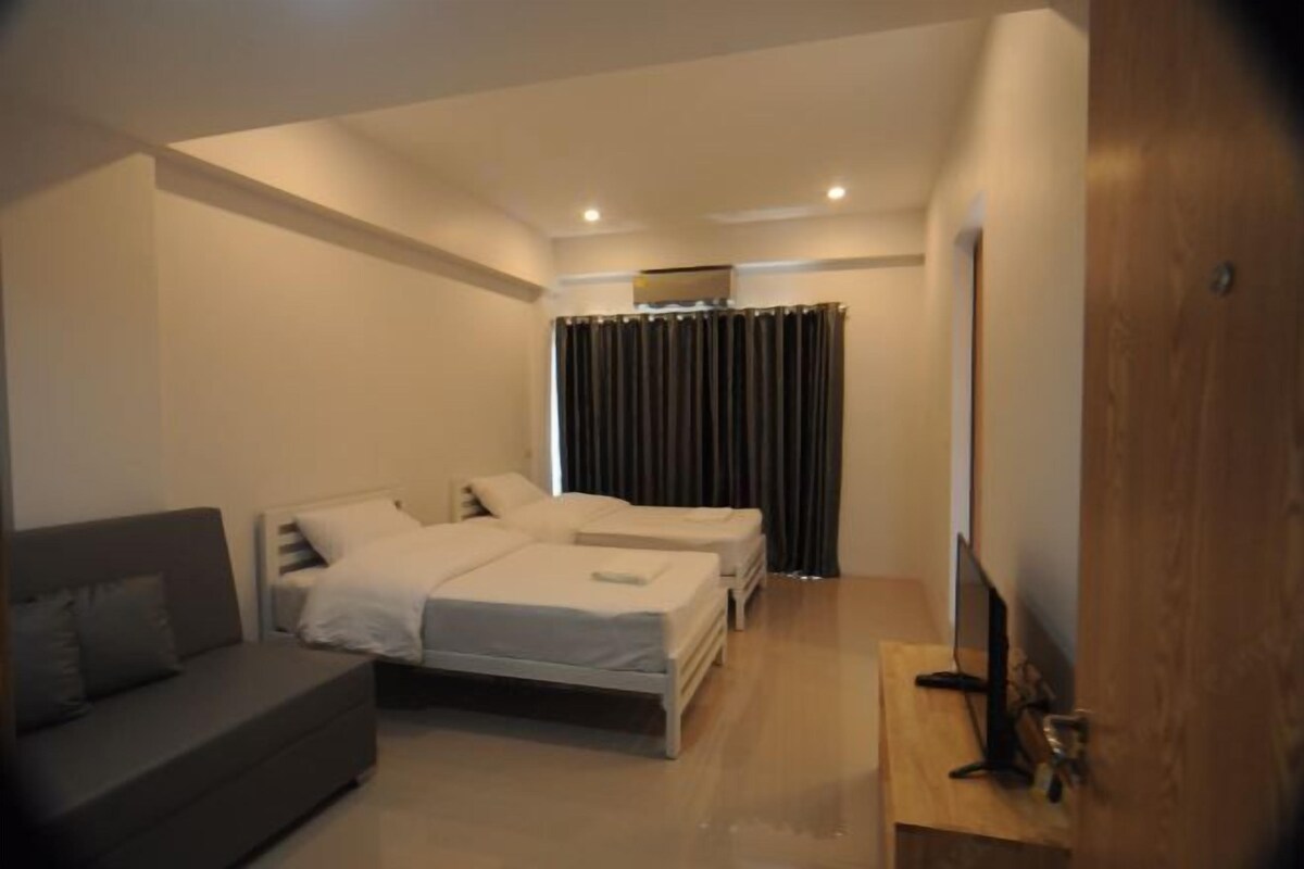 A modern bedroom with a sofa, two single beds, a TV, and a curtain.