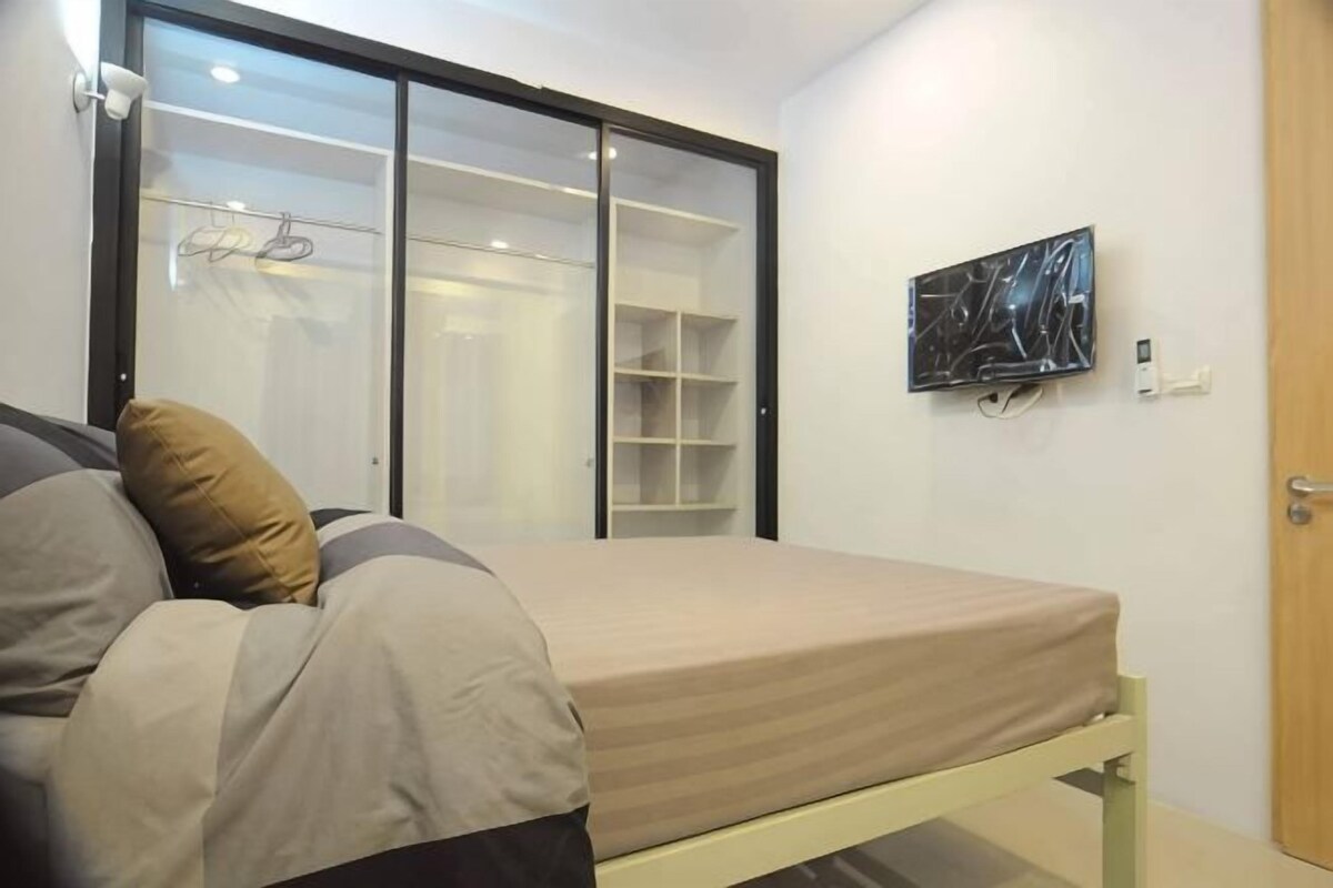 A bedroom with a bed, a wardrobe, a wall-mounted TV, and a door.