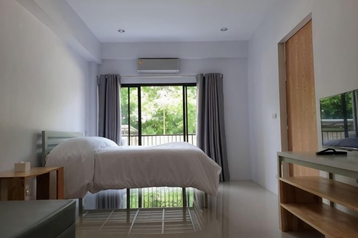 A bedroom with a bed, a TV, a desk, and a window with curtains.