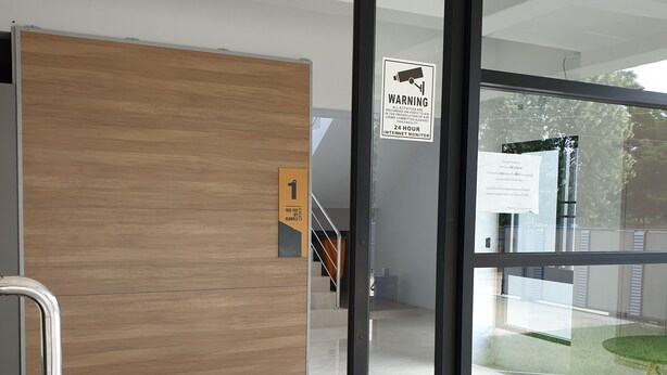 Un interior moderno con un vidrio corredizo que da a una escalera, un panel de pared de madera y un letrero que indica un monitor de internet las 24 horas.