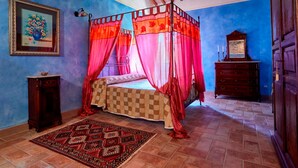 A bedroom with a four-poster bed, a checkered bedspread, a red and orange canopy, a patterned rug, a wooden dresser, and a painting on the wall. - In the middle of nature Apartment. Fireplace and Olives trees view. Zaffiro (Spoleto)
