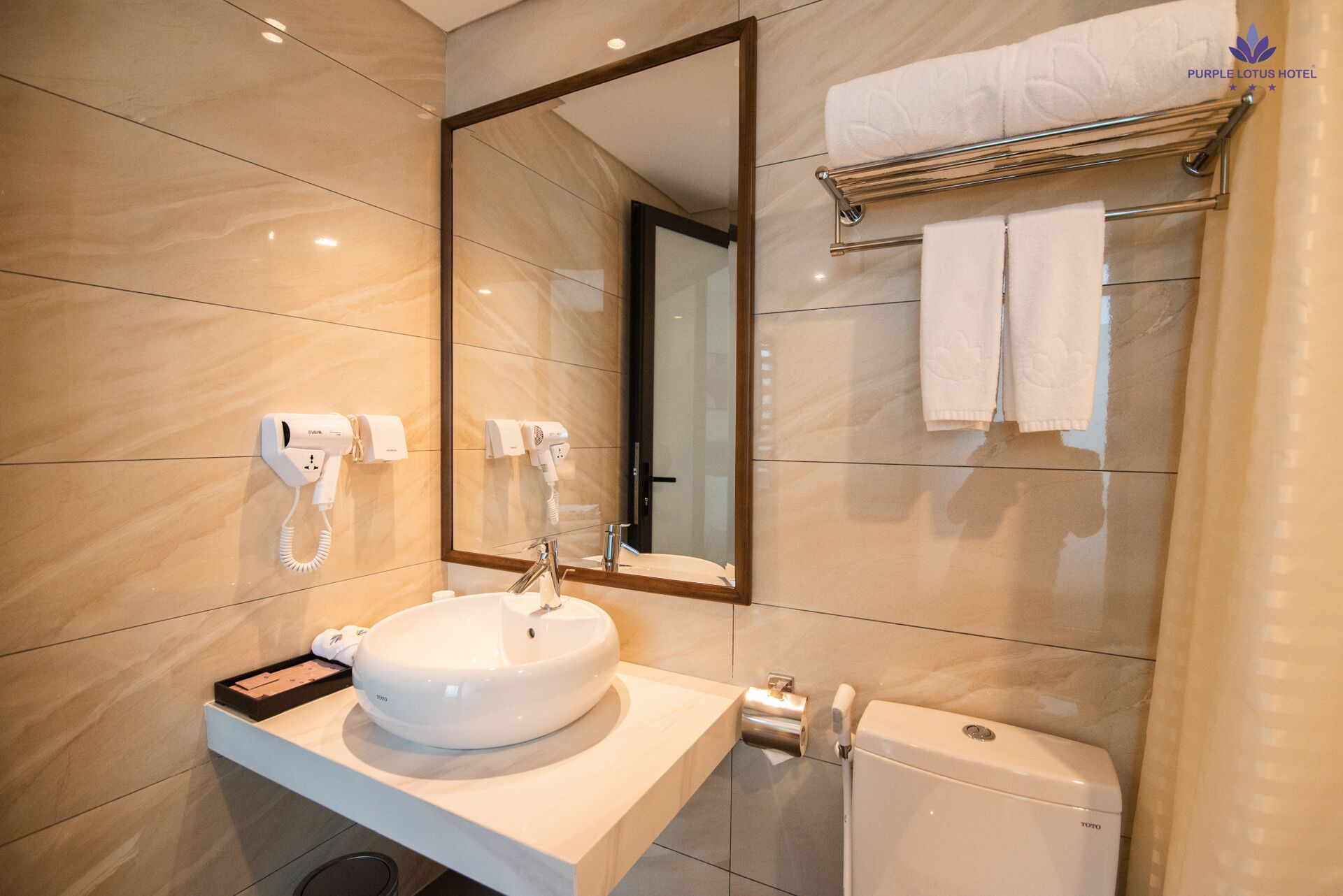 A modern bathroom with a large mirror, a sink, a toilet, and two hair dryers mounted on the wall.