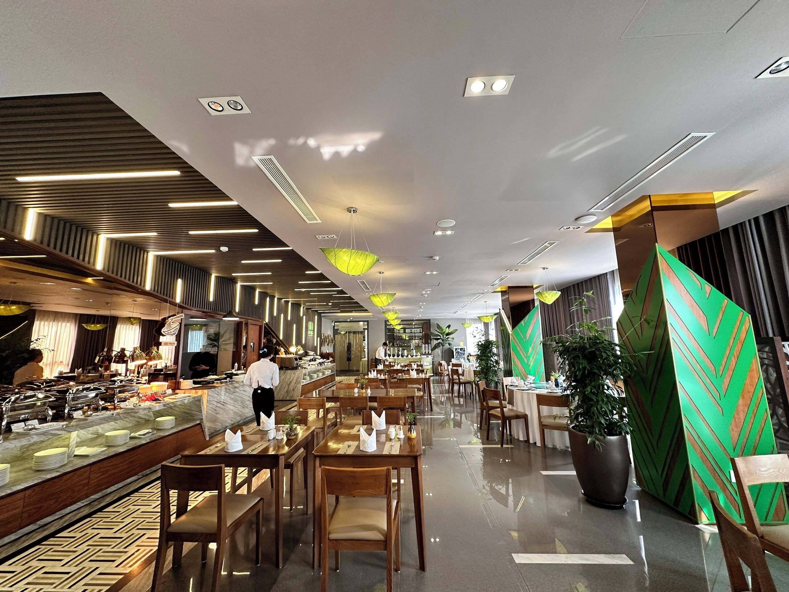 Un hall d’hôtel moderne avec un comptoir d’accueil en marbre, plusieurs tables à manger et une variété de plantes.