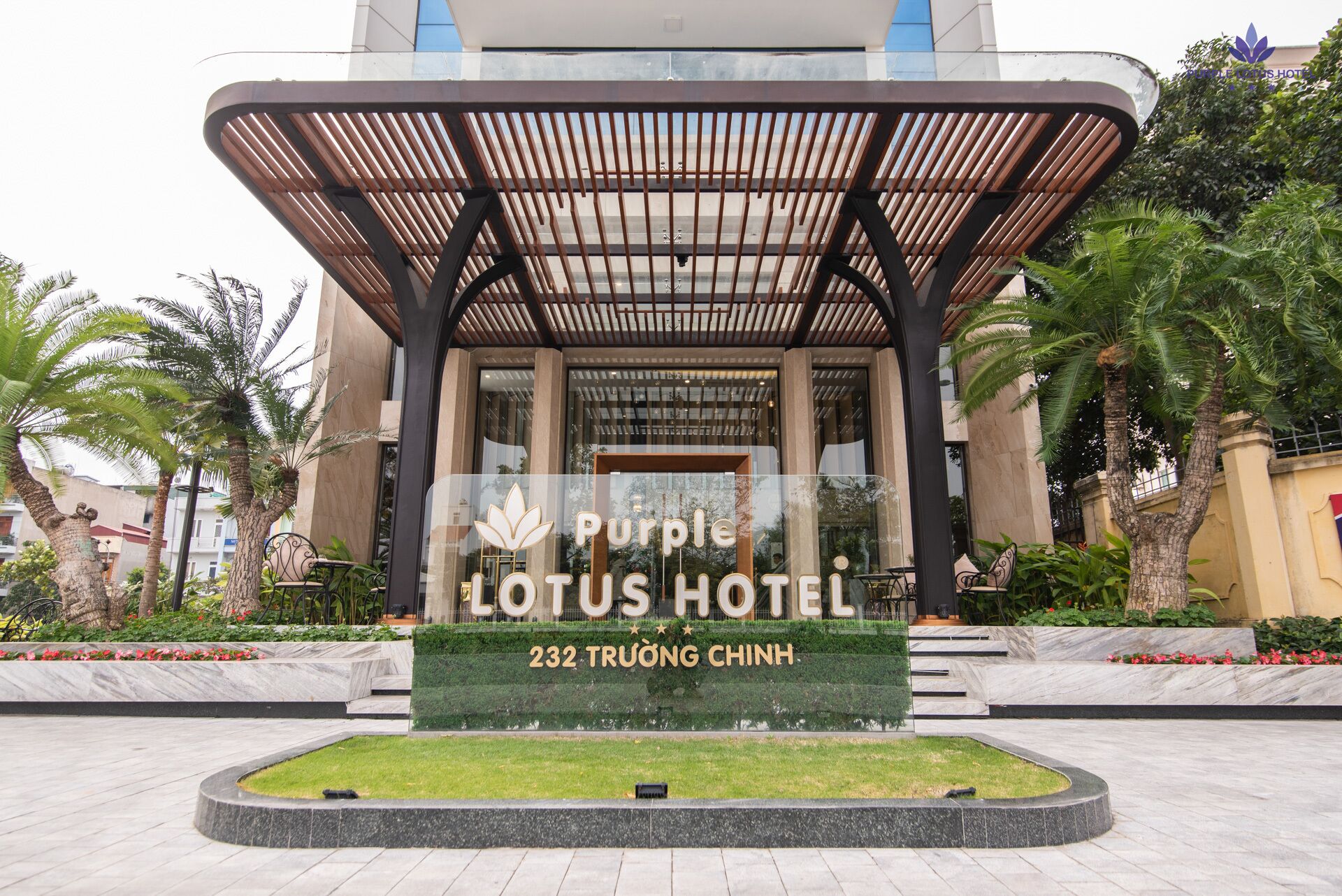 The entrance of the Purple Lotus Hotel with a modern design, featuring a covered entrance and a well-maintained garden area.