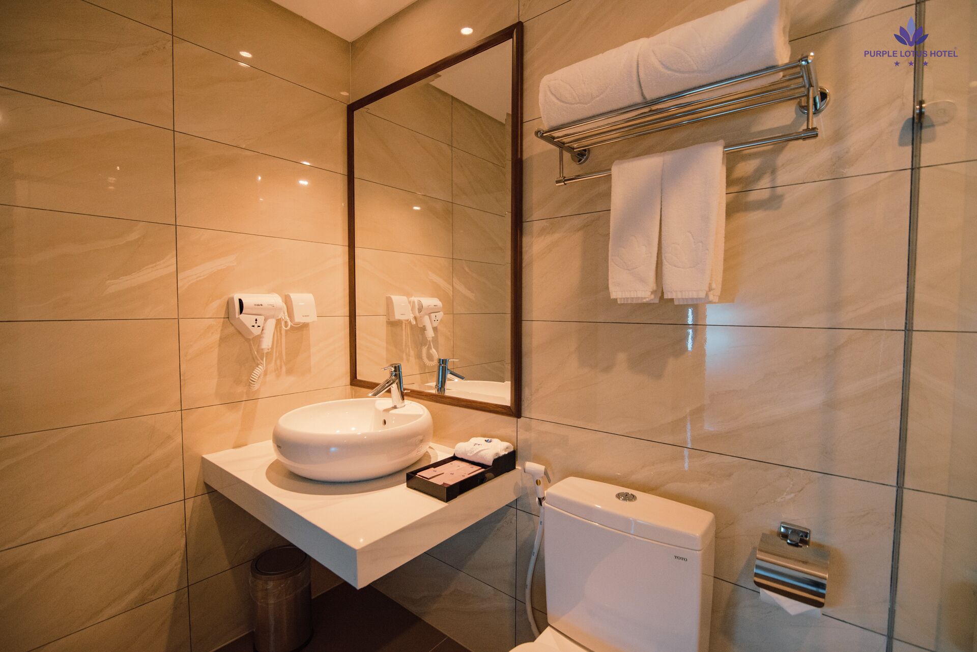 A modern bathroom with a large mirror, a sink, a towel rack, and a toilet.