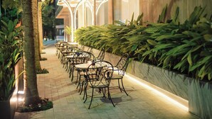 An outdoor dining area with metal chairs and tables, surrounded by greenery and a low wall. - Purple Lotus Hotel (Hai Phong)