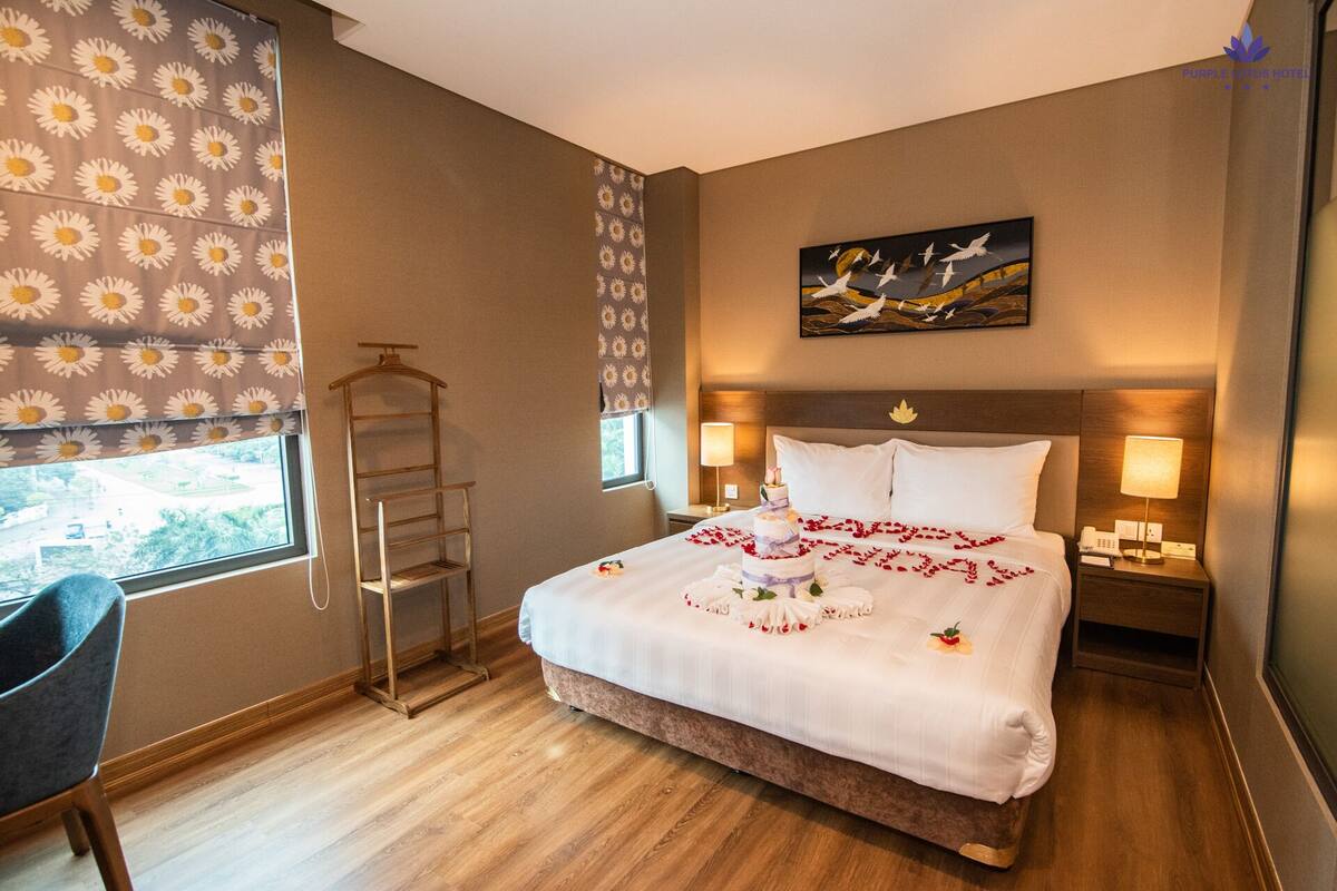 Une chambre d’hôtel avec un lit, des lampes de chevet, une fenêtre donnant sur un paysage agréable, une chaise et un plancher en bois.