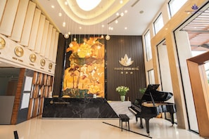 A hotel reception area with a grand piano, a clock, and a wall with floral artwork.
