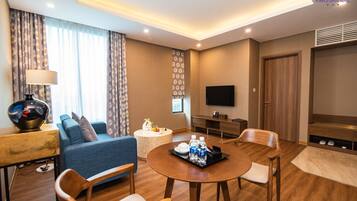 Una habitación de hotel moderna con sofá, una mesa de centro, una mesa de comedor con sillas, un televisor de pantalla plana y una puerta de madera.